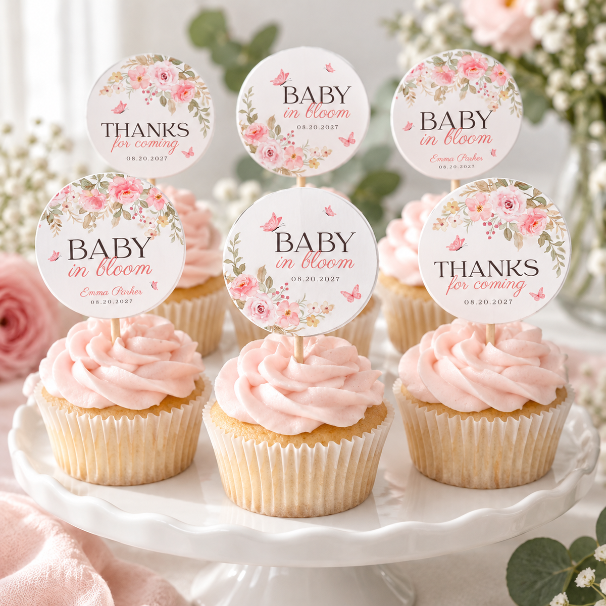 Pink frosted cupcakes on a white cake stand with baby in bloom cupcake toppers