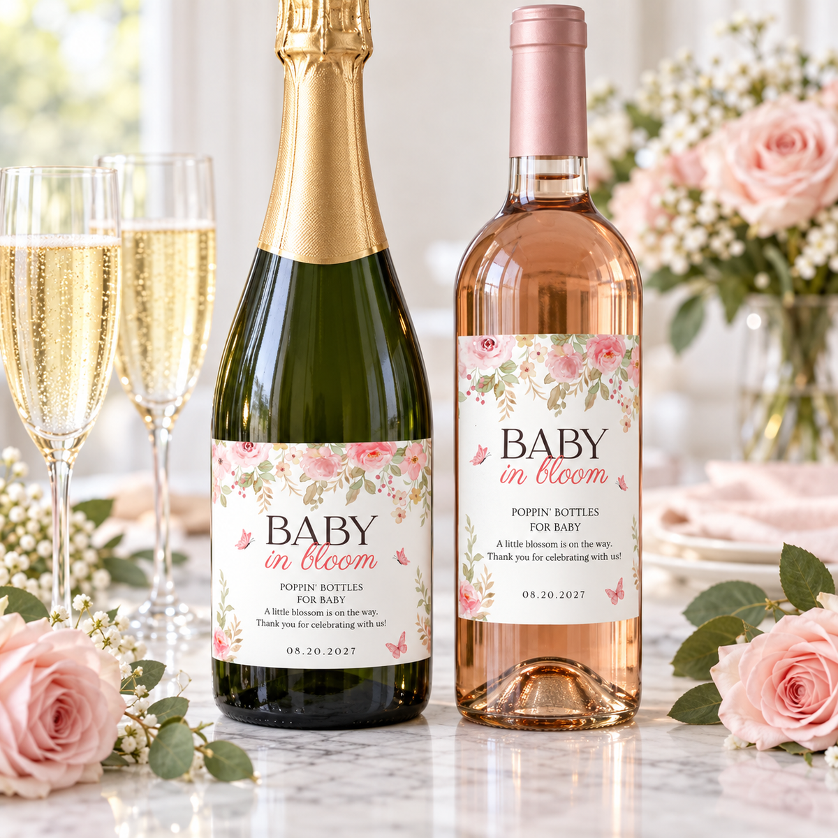 Champagne and wine bottles with baby in bloom labels next to flutes and pink roses
