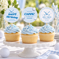 Three golf 1st birthday cupcake toppers on light blue frosted cupcakes on a white cake stand