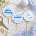 Flat lay of printed golf hole in one cupcake toppers on toothpicks with scissors and a golf ball