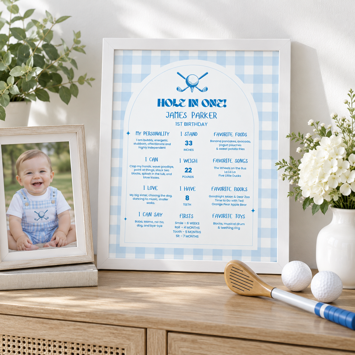 Framed golf first birthday milestone board on a sideboard with a baby photo and golf balls