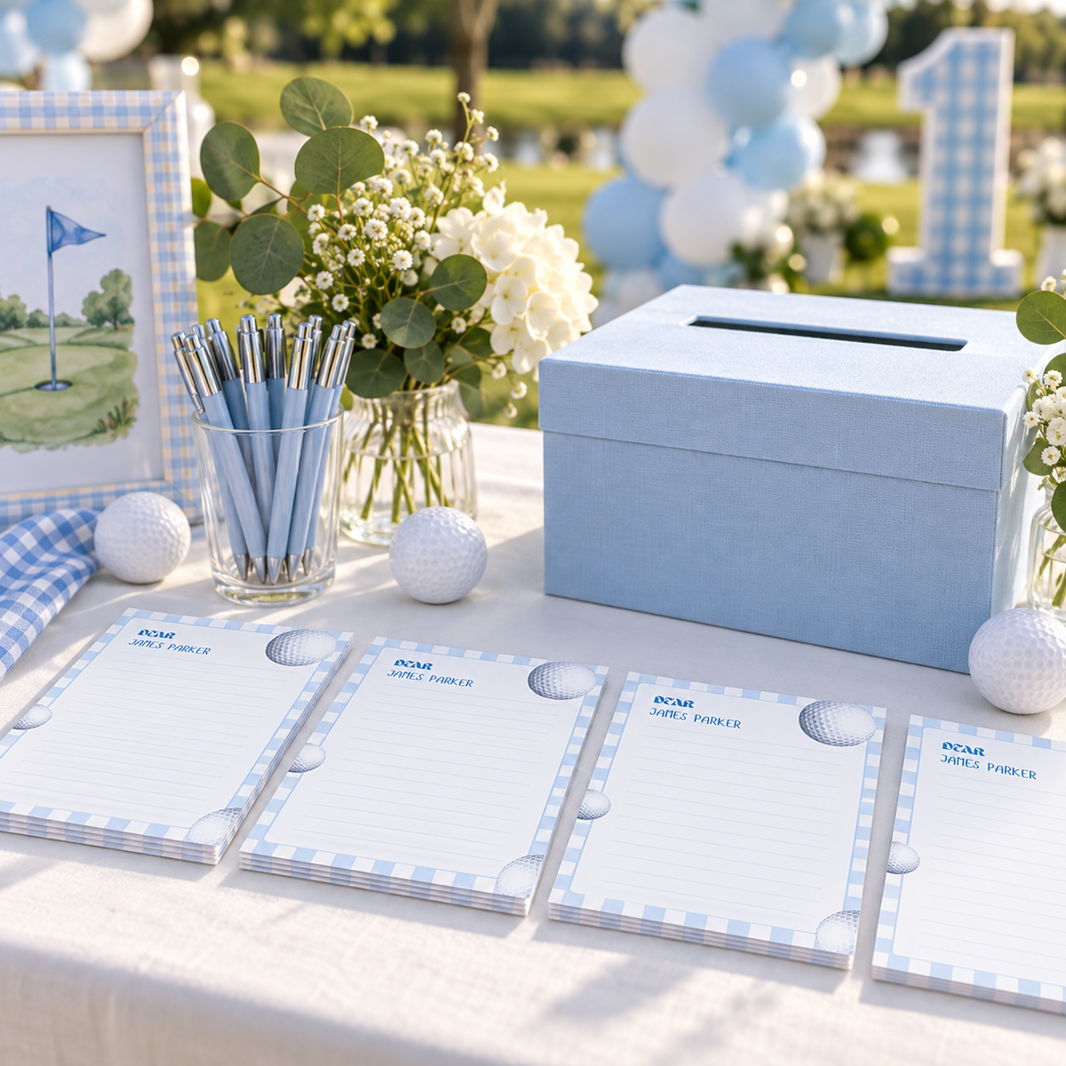 Golf time capsule cards on a guest table with pens and a card box at an outdoor first birthday