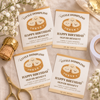 Flat lay of printed little dumpling champagne labels with scissors, tape and a champagne cork