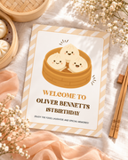 Flat lay of the printable little dumpling 1st birthday welcome sign with chopsticks and a peach ribbon