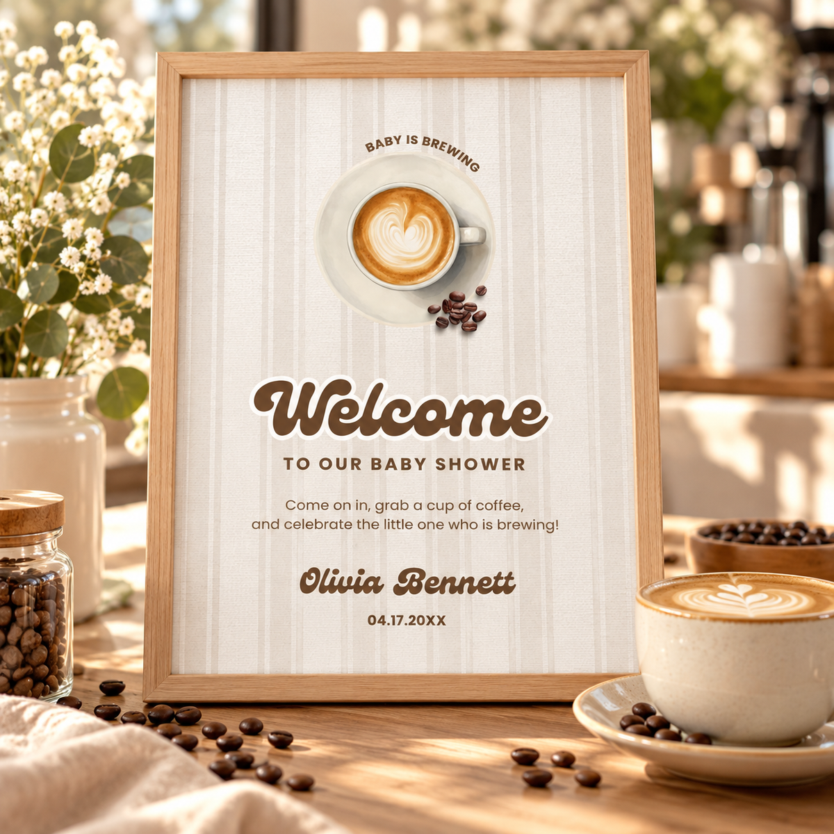 Baby Is Brewing welcome sign in a wooden frame on a table with coffee beans and a latte