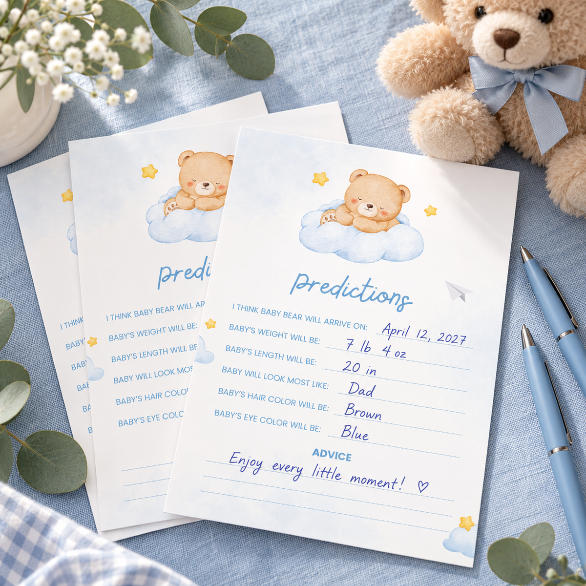 Little Bear baby predictions cards filled in on a blue baby shower table with pens and a teddy bear
