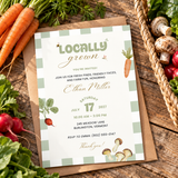 Locally Grown farmers market baby shower invitation on a rustic wooden table with a basket of fresh produce and kraft envelope