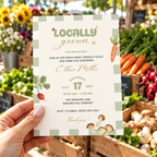 Hand holding the Locally Grown baby shower invitation at a farmers market stall