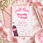 Flat lay of the Ready To Pop baby shower invitation with a blush pink envelope, confetti, ribbon and striped straws