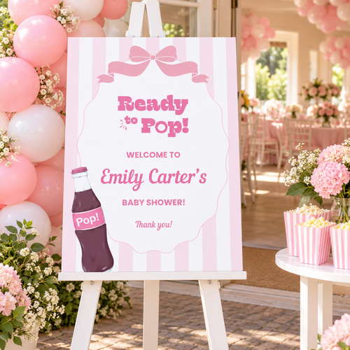 Ready To Pop baby shower welcome sign on an easel at a pink shower entrance with balloons and striped popcorn boxes