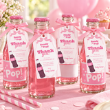 Ready To Pop baby shower favor tags tied with pink ribbon to mini soda bottles on a pink table