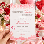 Hand holding the Sweet Little Valentine baby shower invitation at a pink and red party table