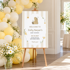 Classic Honey Bear baby shower welcome sign on an easel at the entrance with yellow and cream balloons and daisies