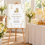 Classic Honey Bear welcome sign on an easel beside a baby shower gift table with honey jars and daisies