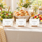 Classic Honey Bear baby shower food labels on wooden stands in front of salad, honey rolls and fruit skewers on a buffet with daisies